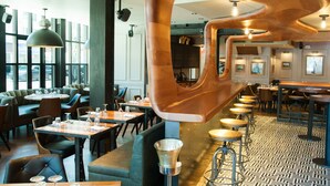 A modern restaurant interior with high ceilings, exposed ductwork, and a mix of seating options including bar stools and booths.