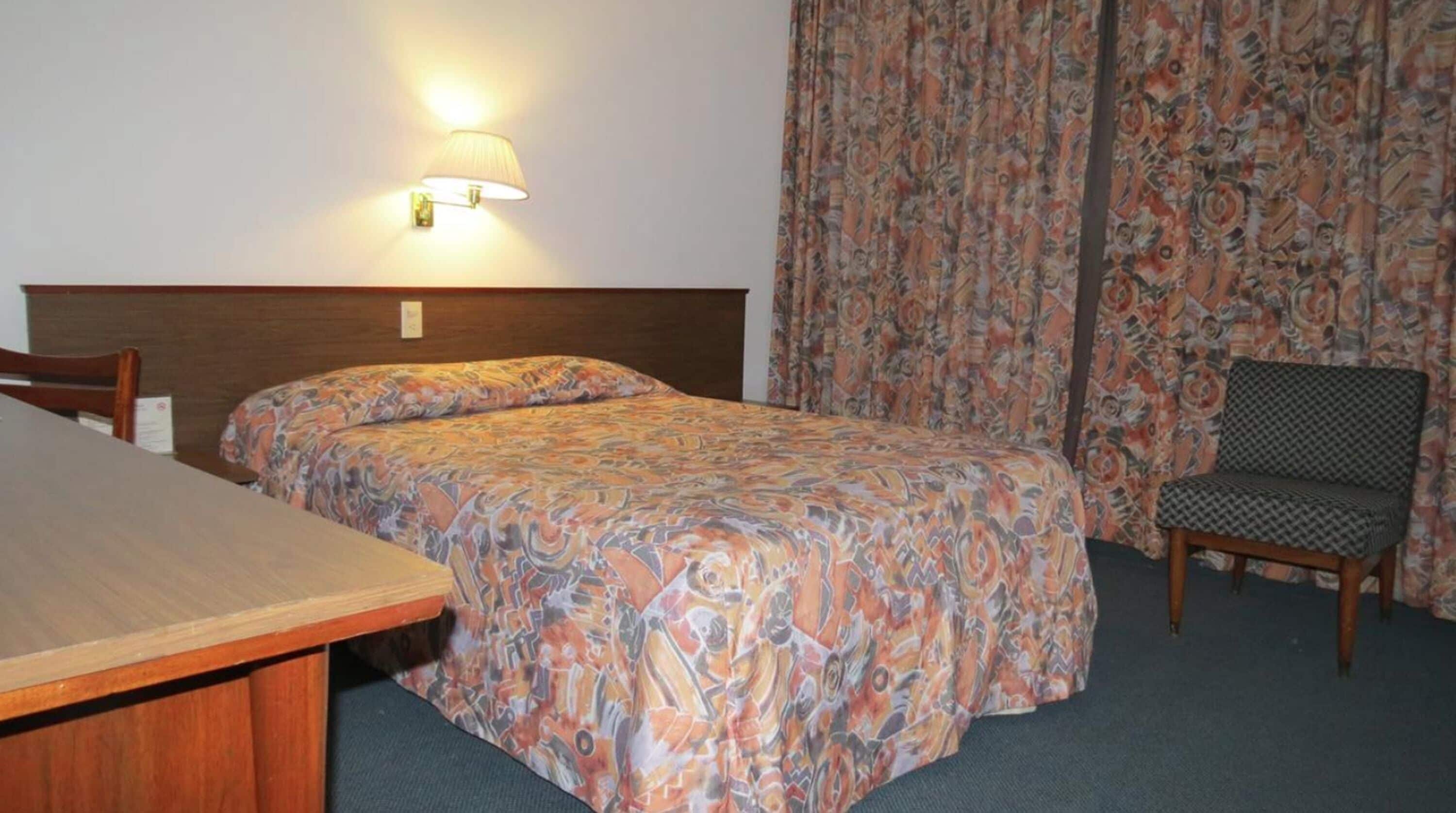 Et hotelværelse med en seng, en stol, et bord og en lampe på væggen.