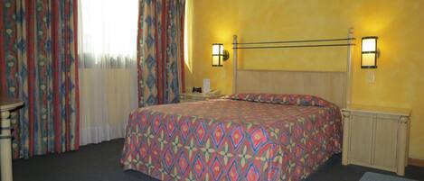 Une chambre d’hôtel avec un lit, des rideaux, une table de chevet et deux lampes fixées au mur.