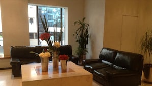 A living room with a coffee table, two black leather sofas, and potted plants. - Hotel Sevilla (Mexico City)