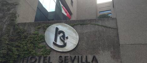 Exterior do Hotel Sevilla, com um logotipo e nome em destaque numa parede de pedra.