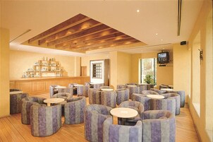 Un'ampia zona lounge con diverse opzioni di seduta, un bar fornito di numerosi alcolici e una televisione a parete.