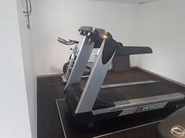Una cinta de correr en una habitación con piso alfombrado y pared lisa.