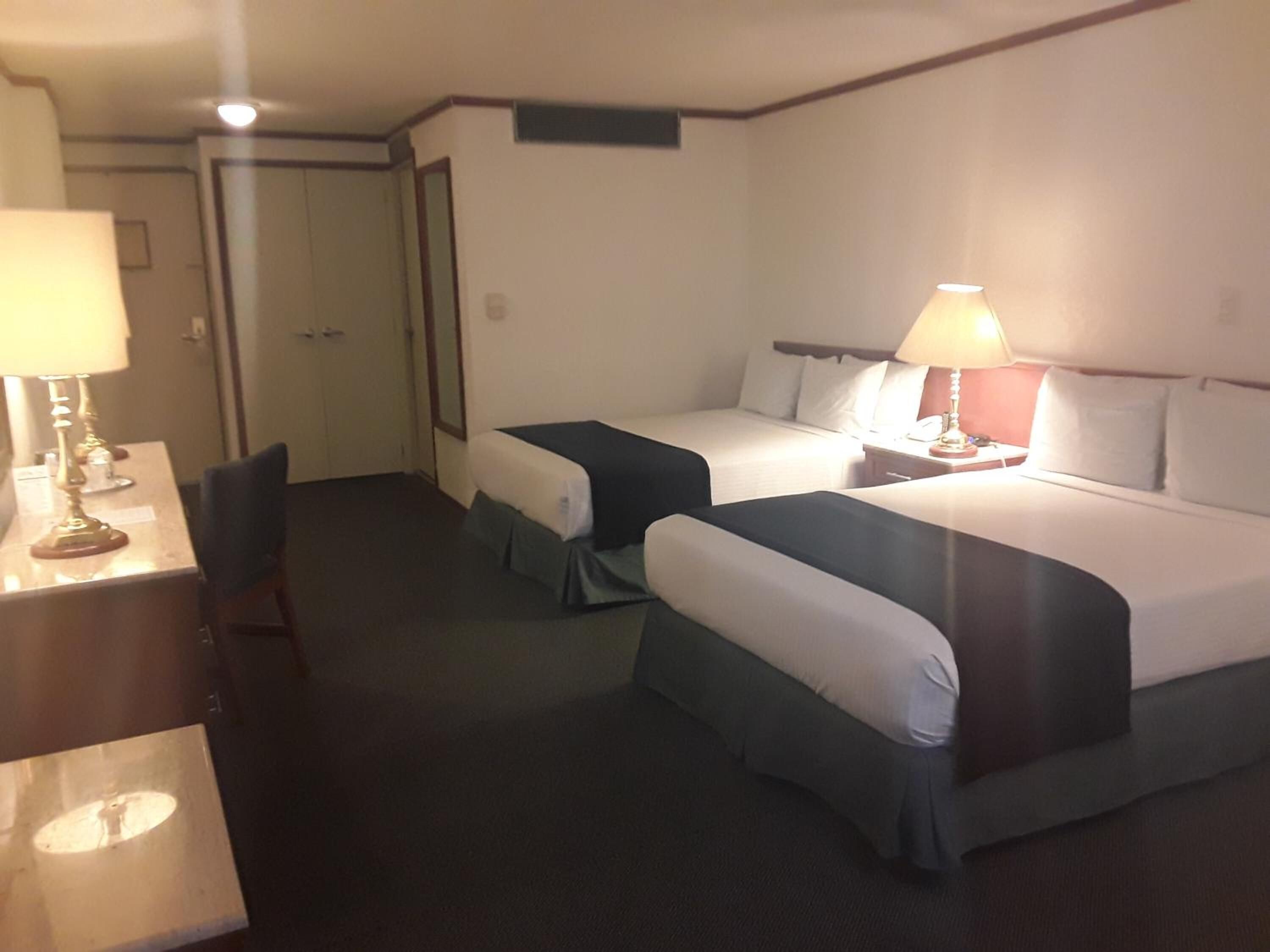A hotel room with two beds, a desk, and two lamps.