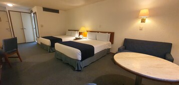 Una habitación de hotel con dos camas, una mesa redonda, una silla y una lámpara.