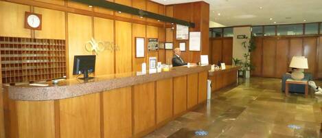 A reception desk with a wooden finish, a clock, and a computer monitor.
