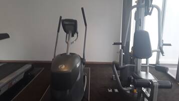 Un gimnasio con cinta de correr, elíptica y máquina de pesas.
