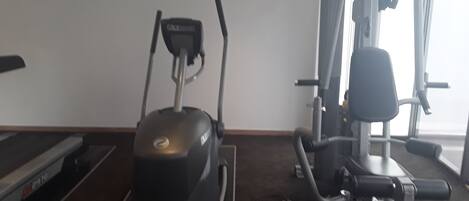 Un gimnasio con cinta de correr, elíptica y máquina de pesas.