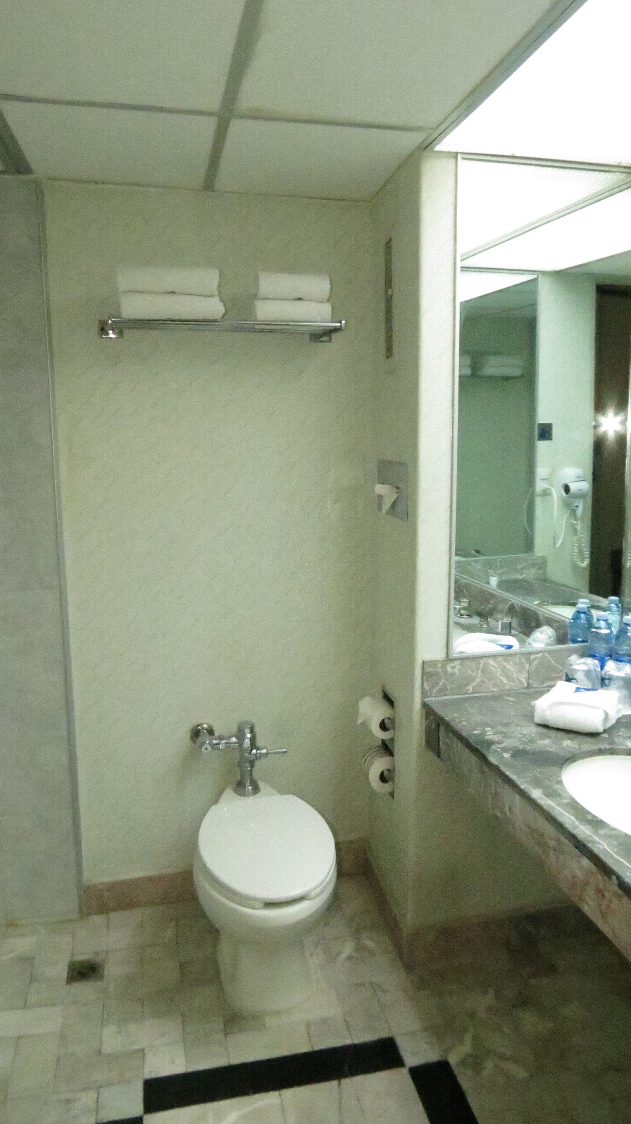 A bathroom with a toilet, a sink, and a mirror. There are two shelves with towels above the toilet.