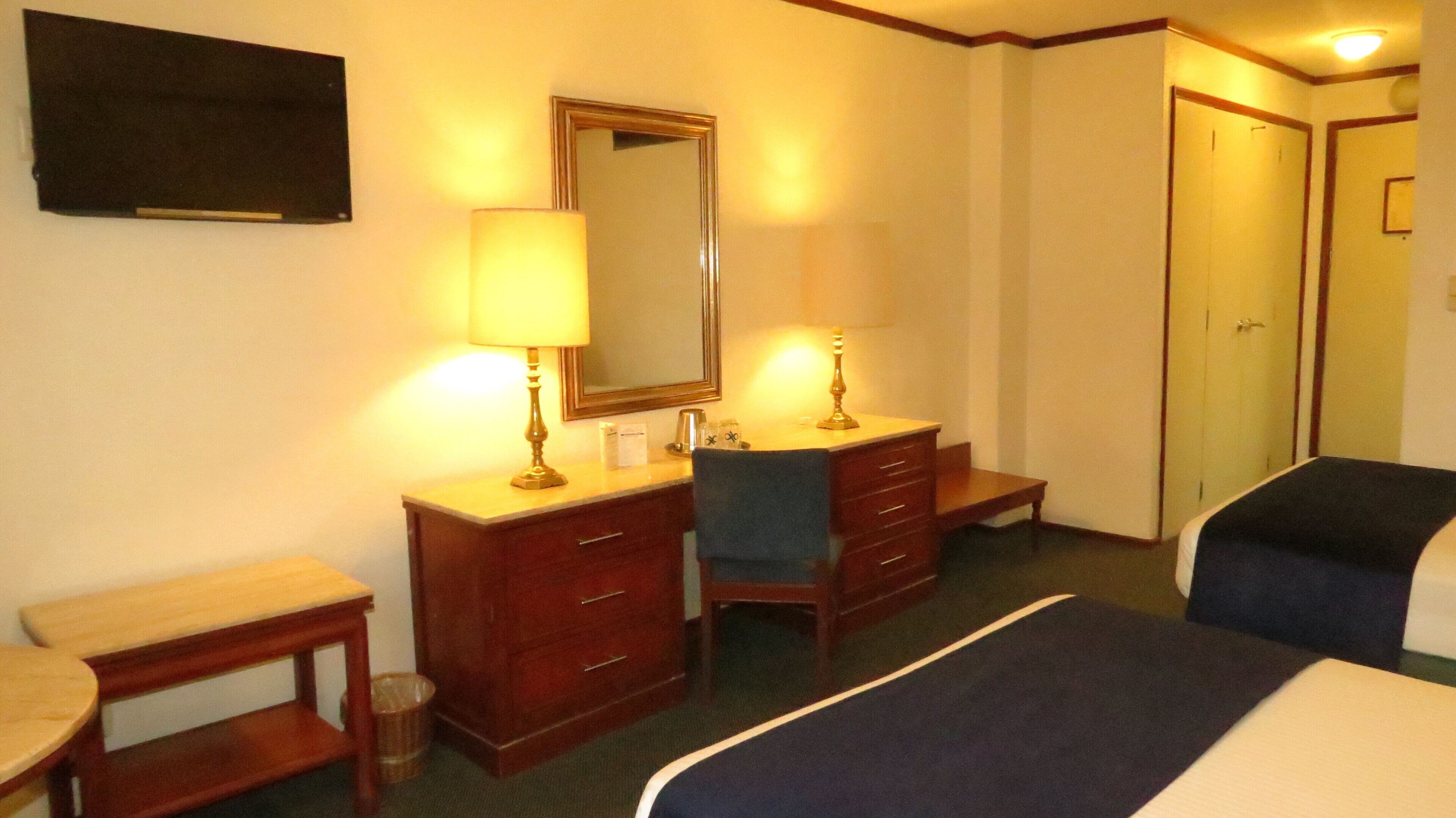 Habitación de hotel con cama, escritorio, silla, cómoda, espejo y armario.