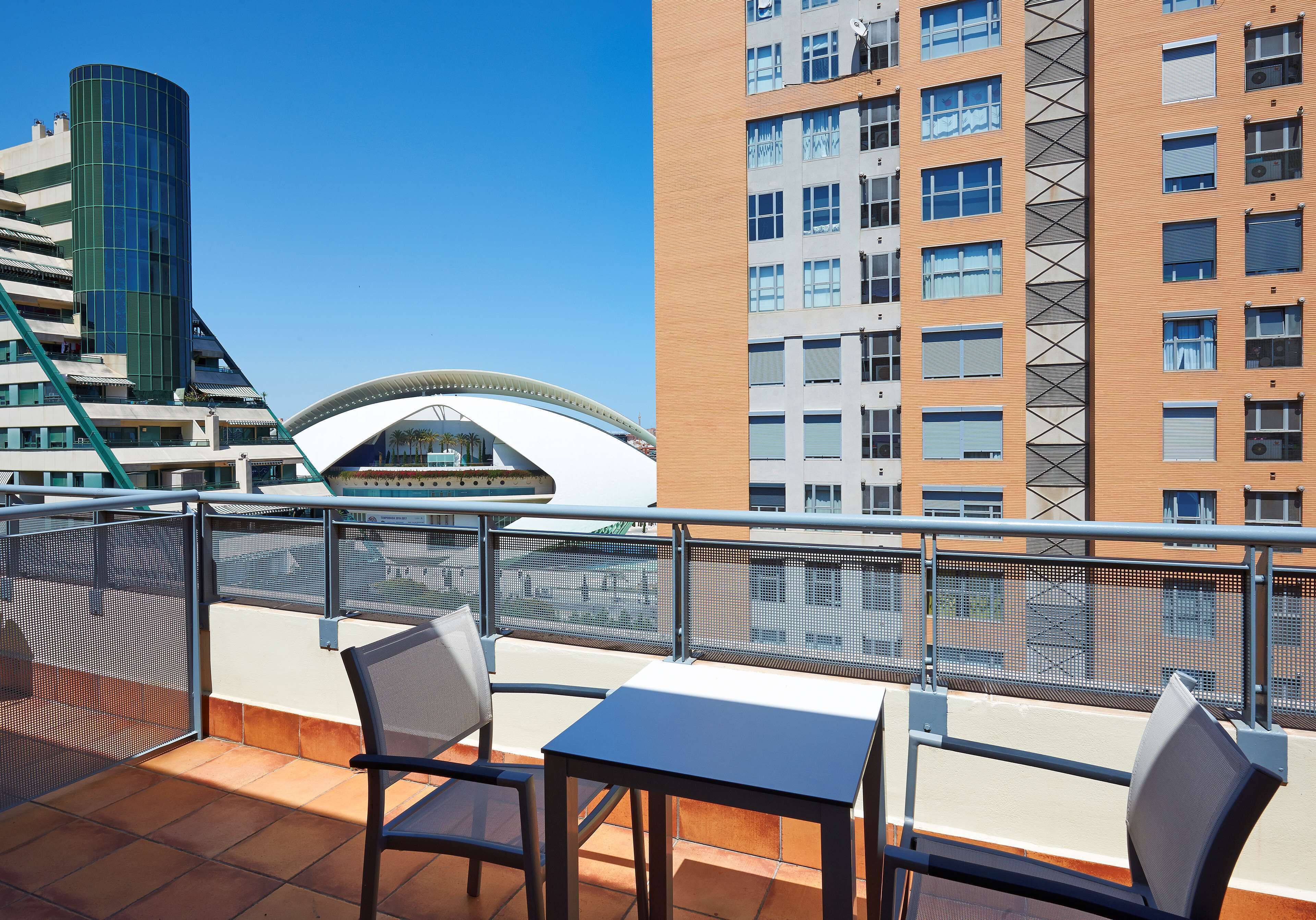 Un balcone con tavolo e sedie, vista su un edificio moderno e un ponte.