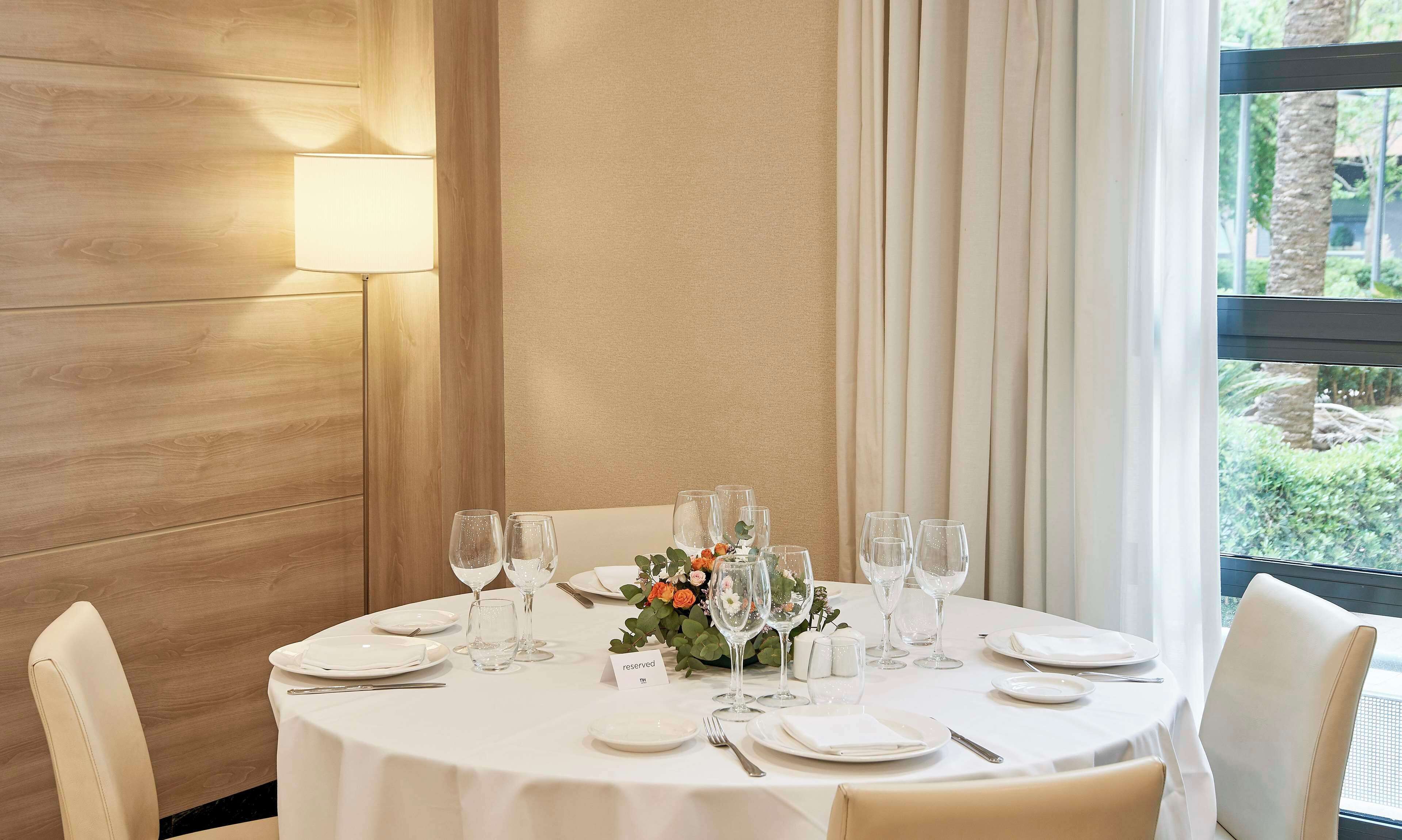 A round dining table with white tablecloth, set with plates, glasses, and a floral centerpiece.