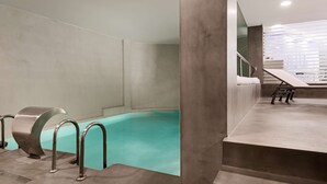Un área de piscina interior moderna con superficie de agua cristalina, paredes de concreto y diseño minimalista.