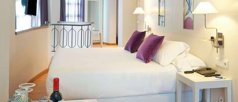 A hotel room with a bed, bedside table, lamp, and a small desk with a telephone and a bottle.