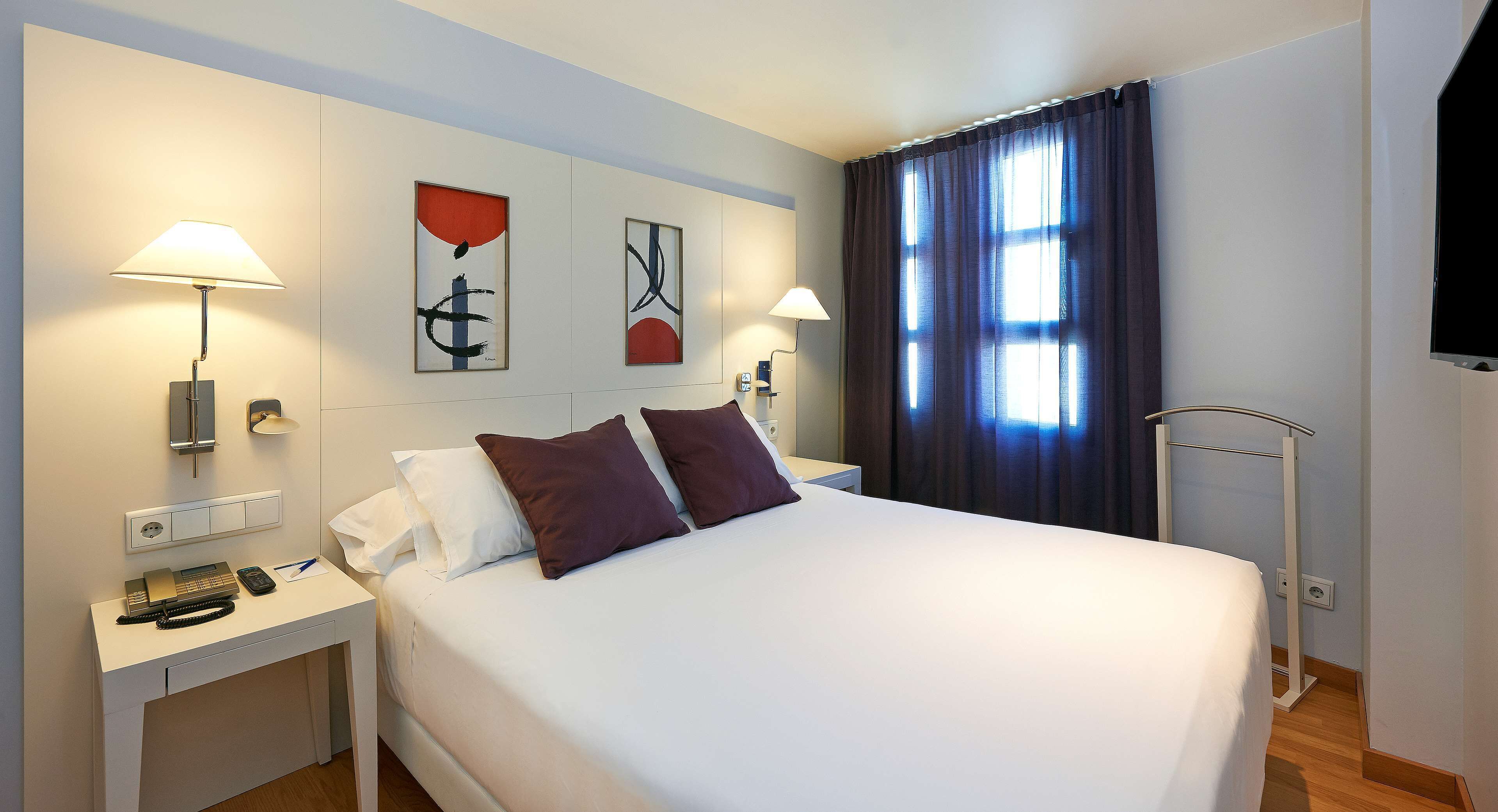 Une chambre d’hôtel avec un lit, deux lampes de chevet, un téléphone et des œuvres d’art accrochées au mur.