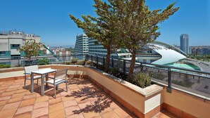 Una terraza en la azotea con una mesa, sillas, un árbol y vistas de la ciudad.