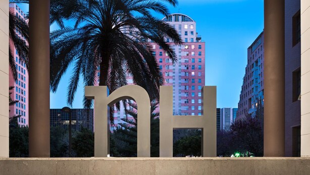 Un gran letrero de 'nh' al frente, con vista a altos edificios y palmeras en el fondo.