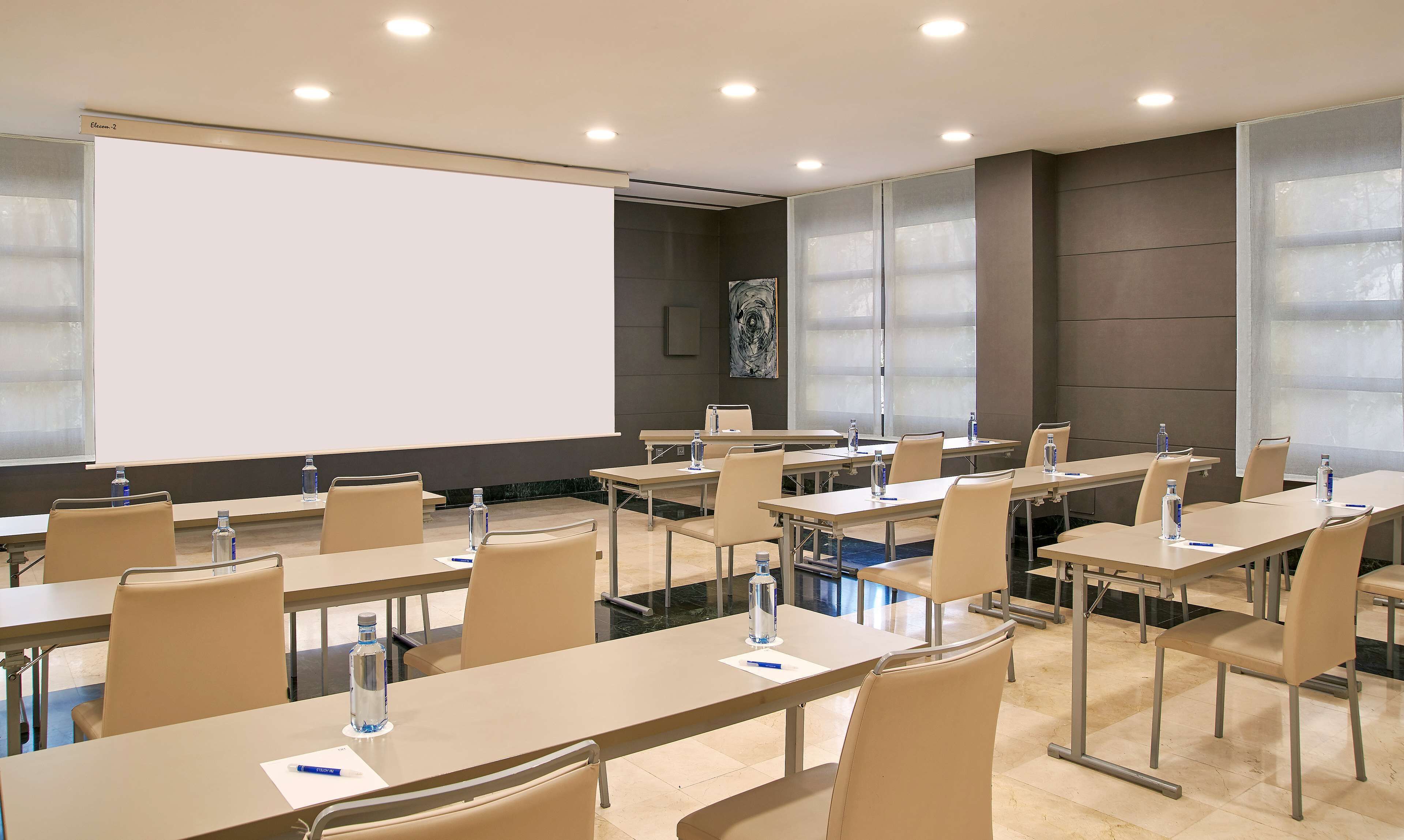 A conference room with tables, chairs, a projector screen, and a large window.