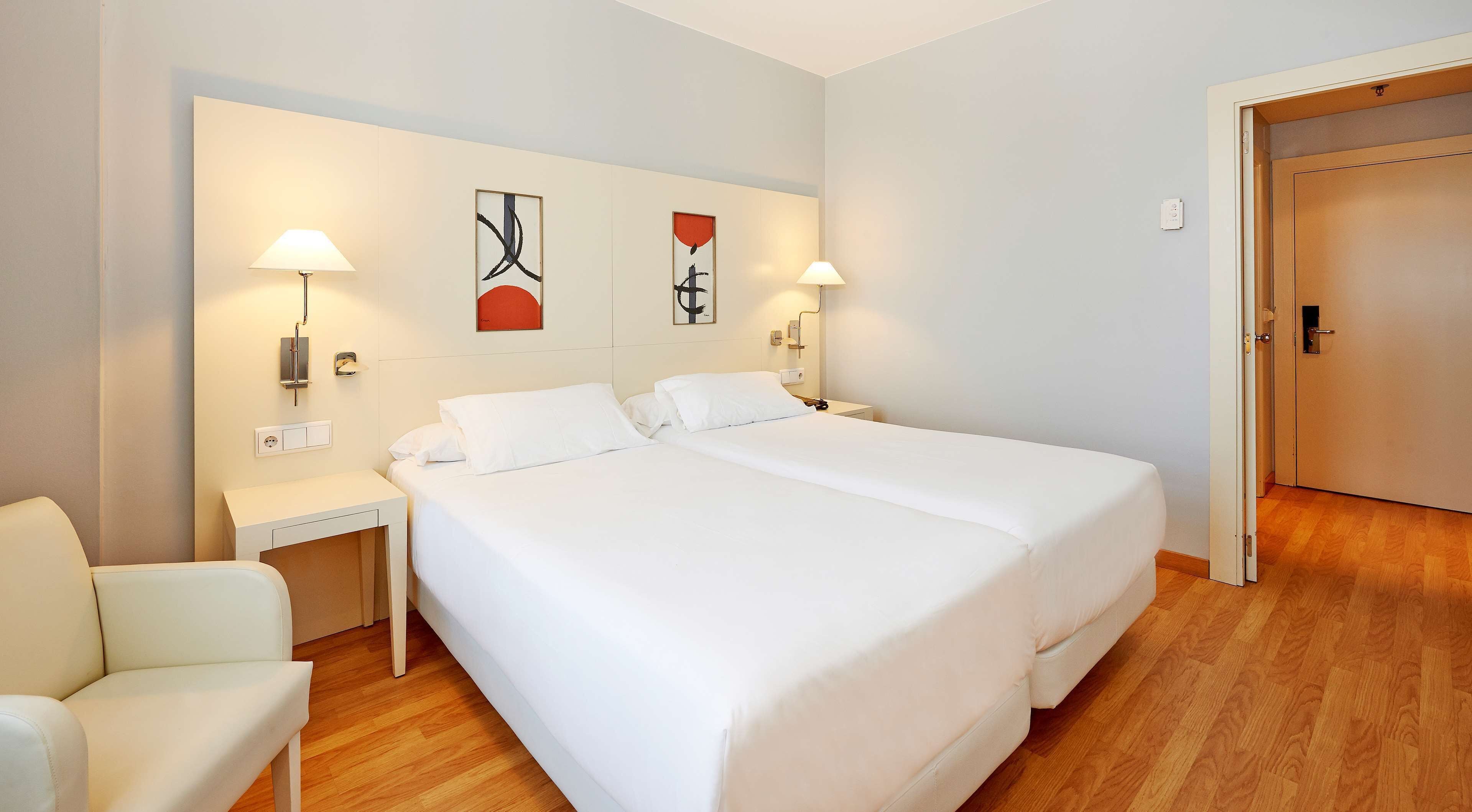 A hotel room with two beds, a chair, and artwork on the wall.