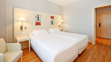 A hotel room with two beds, a chair, and artwork on the wall.