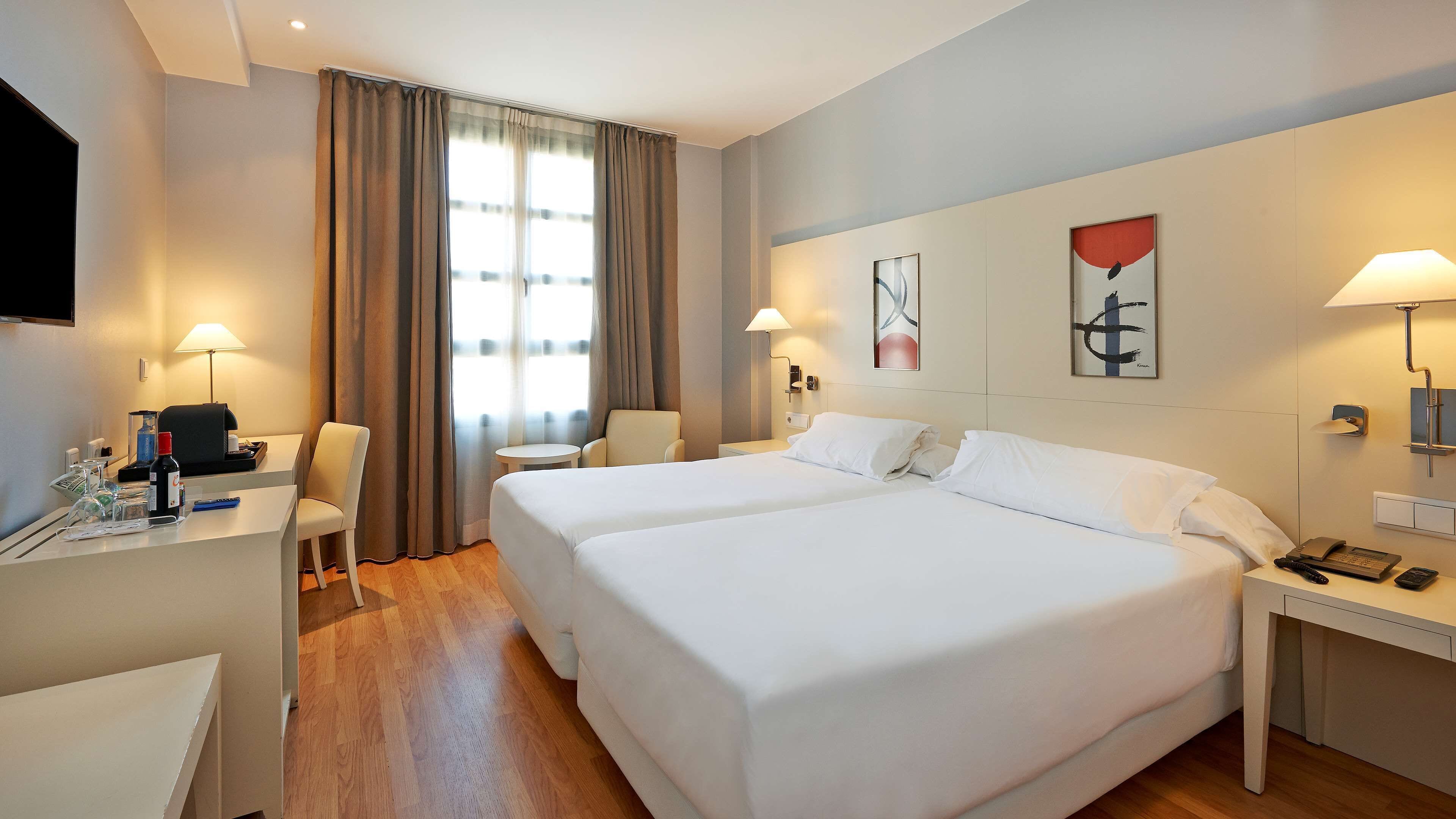 A hotel room with two beds, a desk with a chair, a telephone, and a lamp.