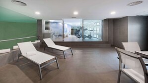 Un área de espera moderna con sillones reclinables, un separador de vidrio y vistas a un gimnasio.