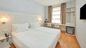 A hotel room with a large bed, a desk, a chair, a small fridge, a mirror, and a TV. - NH Valencia Las Ciencias Hotel (Valencia)