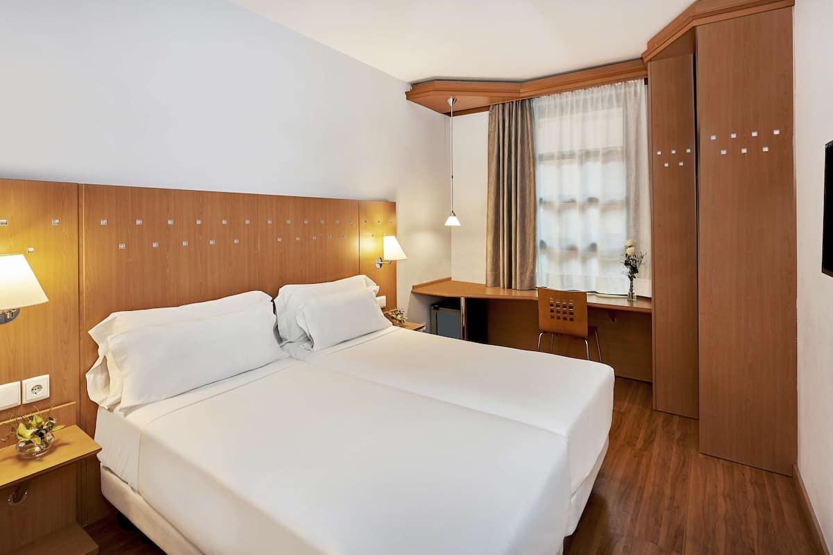 A hotel room with a large bed, bedside lamps, a desk, a mirror, and a TV.
