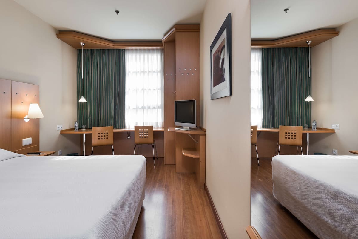 A hotel room with two beds, a desk with a computer, a chair, and a TV.