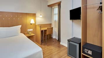 A hotel room with a bed, desk, chair, TV, and a small heater.