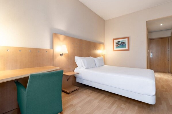 A hotel room with a bed, a desk, a chair, and a wall-mounted lamp. - Crisol Leganés (Leganes)