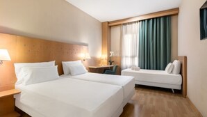 A hotel room with two beds, a desk, a chair, and a window with curtains. - Crisol Leganés (Leganes)
