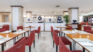 A modern dining area with red chairs and wooden tables, equipped with self-service coffee machines and a counter with a menu display. - Crisol Leganés (Leganes)