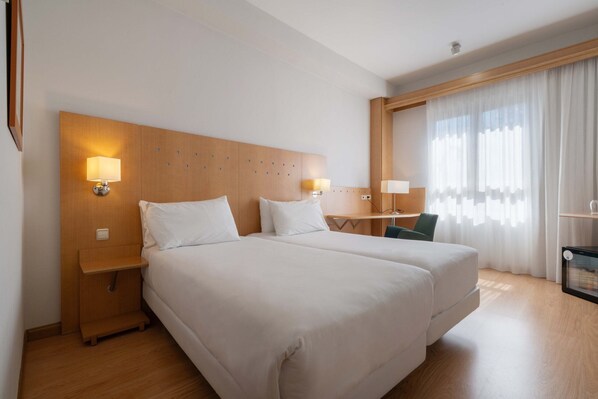 A hotel room with two beds, wooden headboard, bedside lamps, a desk, and a chair. - Crisol Leganés (Leganes)