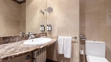Un baño con lavamanos de mármol, un espejo, un perchero para toallas y un inodoro.