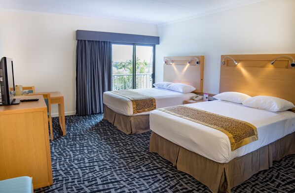 Two single beds with throw blankets, a desk, and a large window offering a view of palm trees.