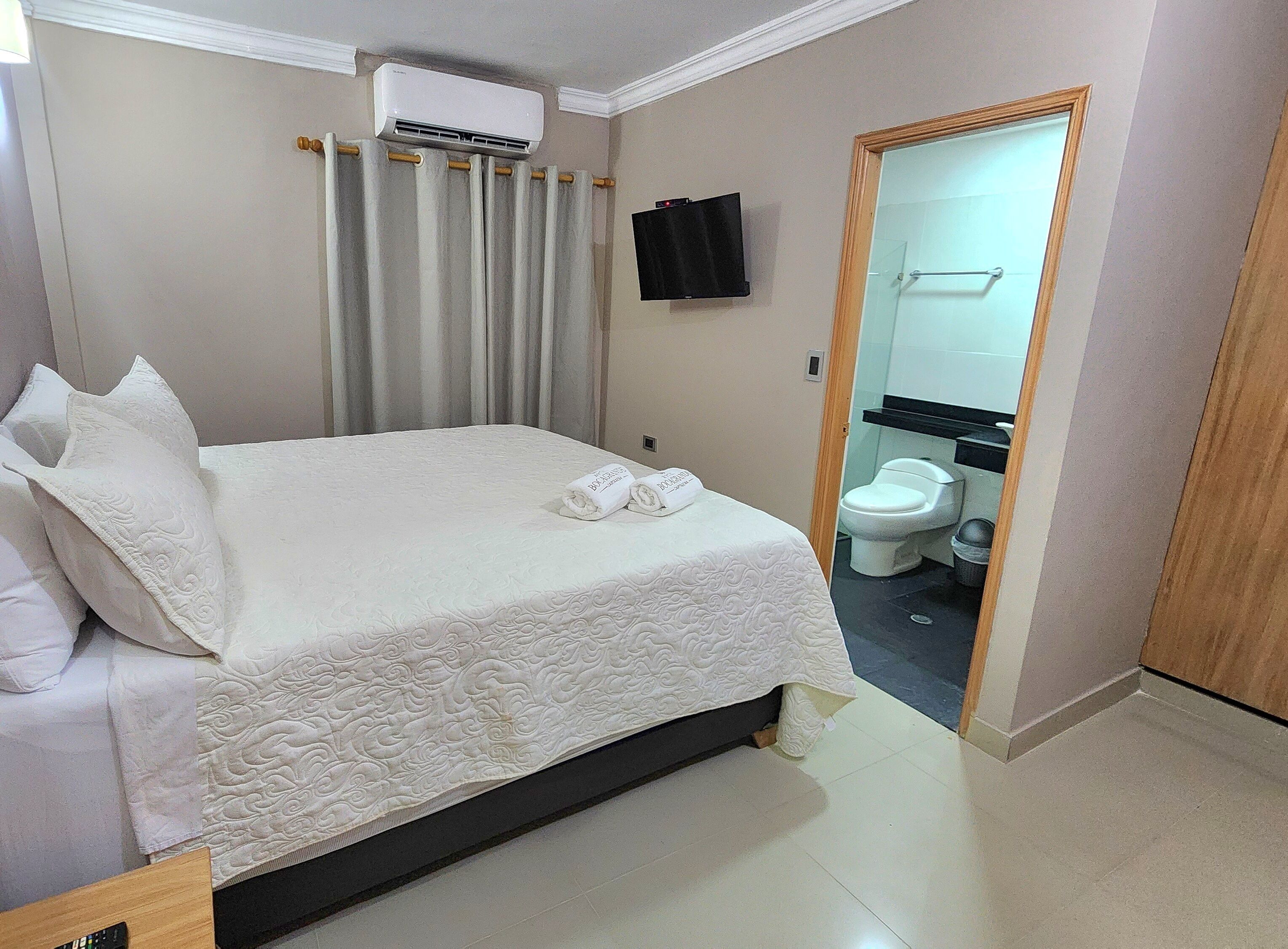 Ein Hotelzimmer mit einem Bett, einer Klimaanlage, einem Fernseher und einem durch eine geöffnete Tür einsehbarer Badezimmer.
