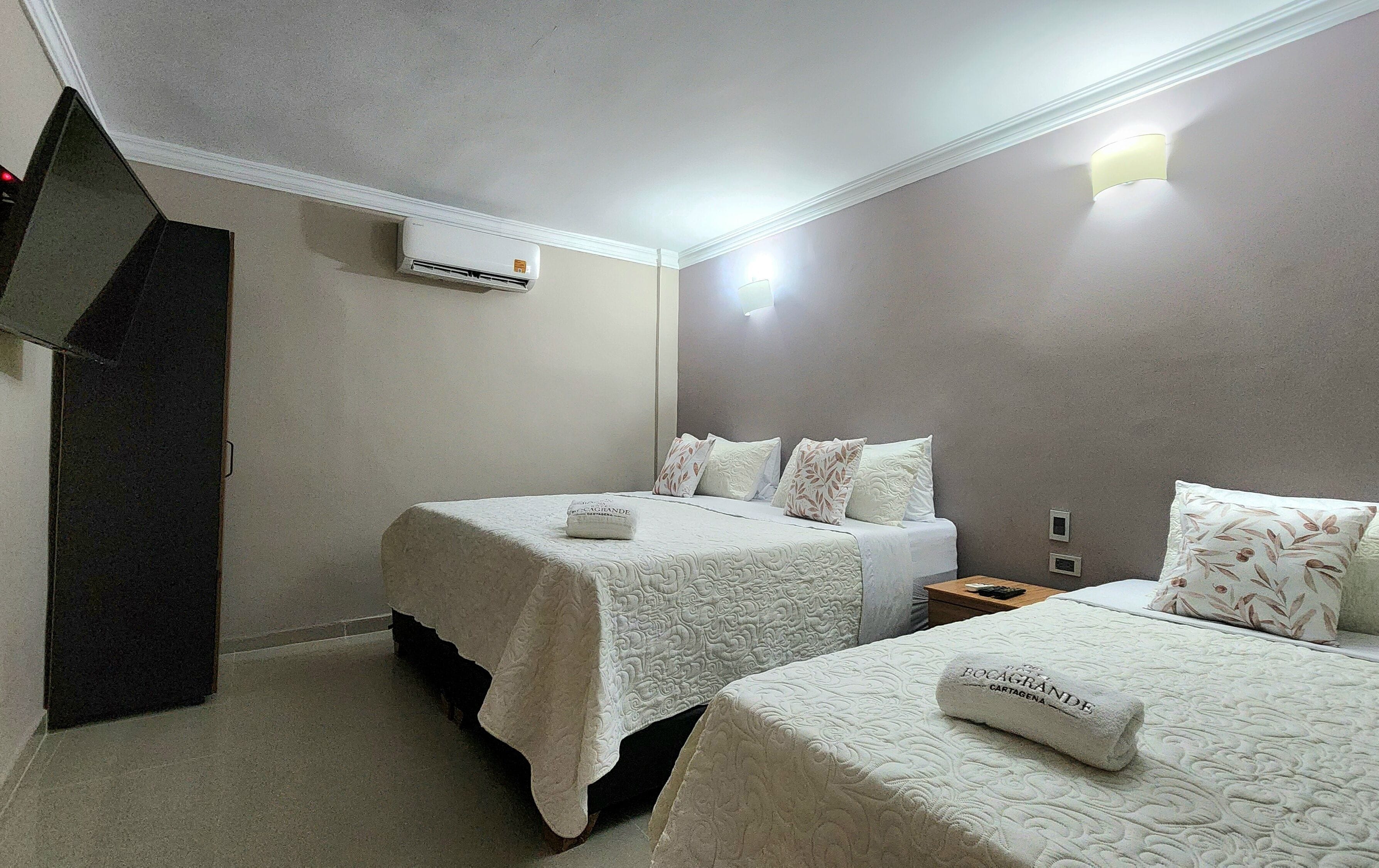 A hotel room with two beds, a flat-screen TV, an air conditioner, and a nightstand with a lamp.
