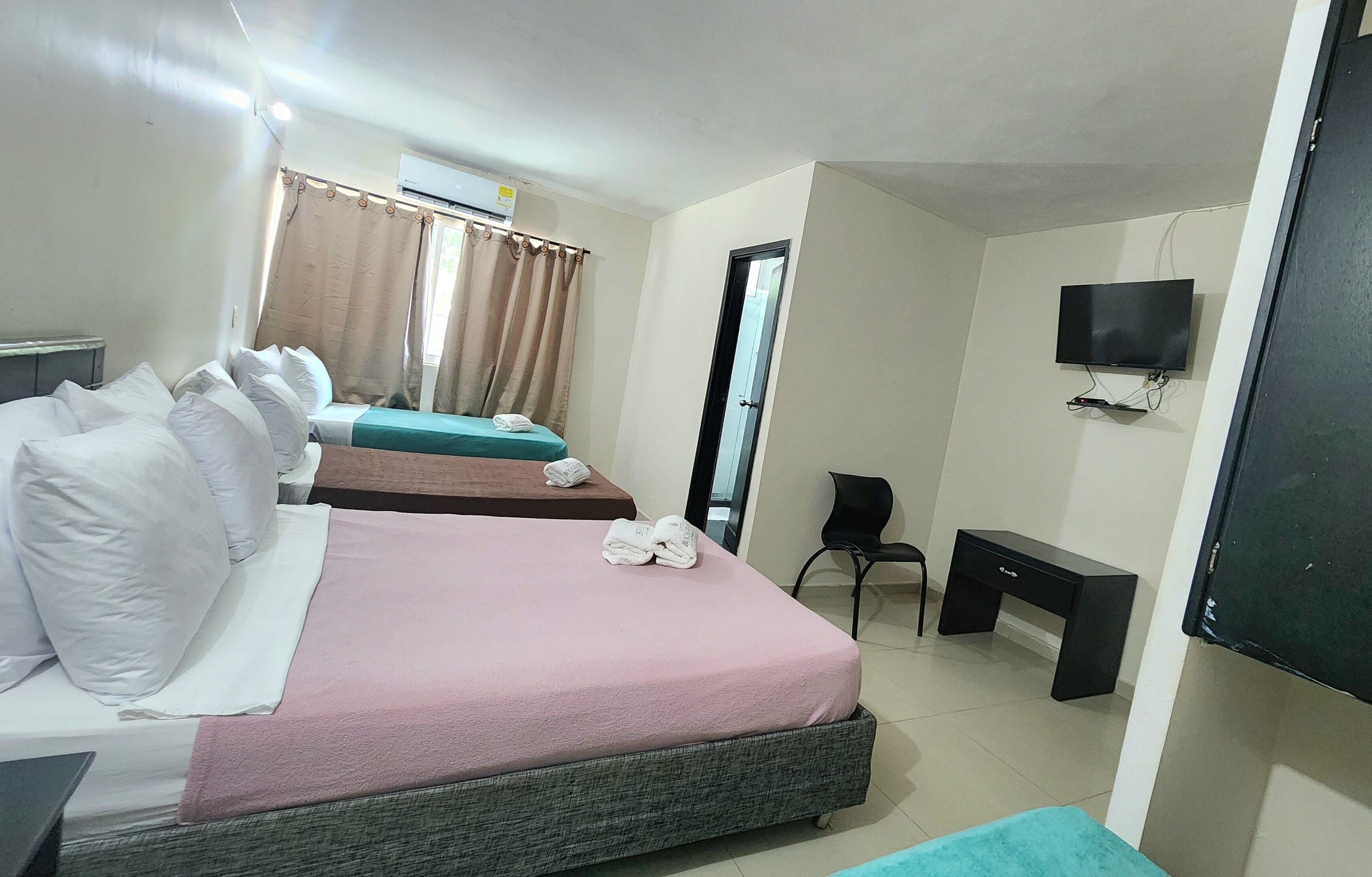Ein Hotelzimmer mit zwei Betten, einem Schreibtisch, einem Stuhl, einem Fernseher und einer Klimaanlage.
