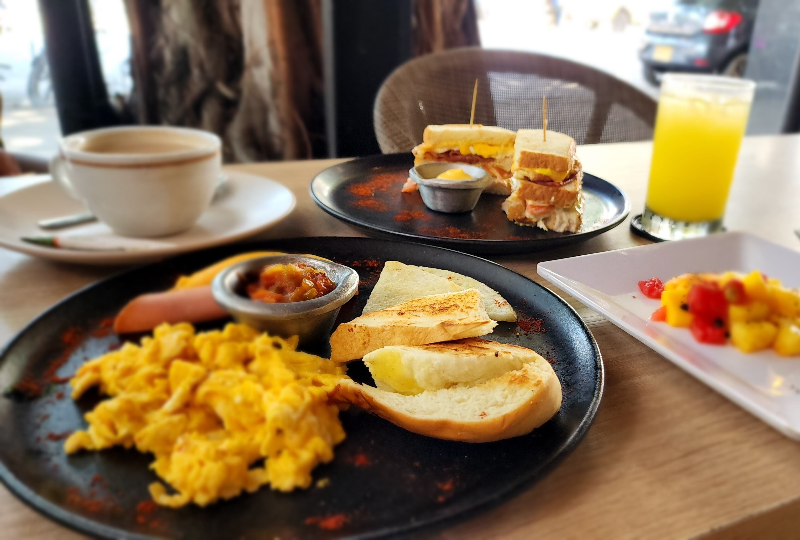 En måltid bestående av rörägg, rostat bröd och en smörgås på en tallrik, en kopp kaffe och ett glas apelsinjuice.