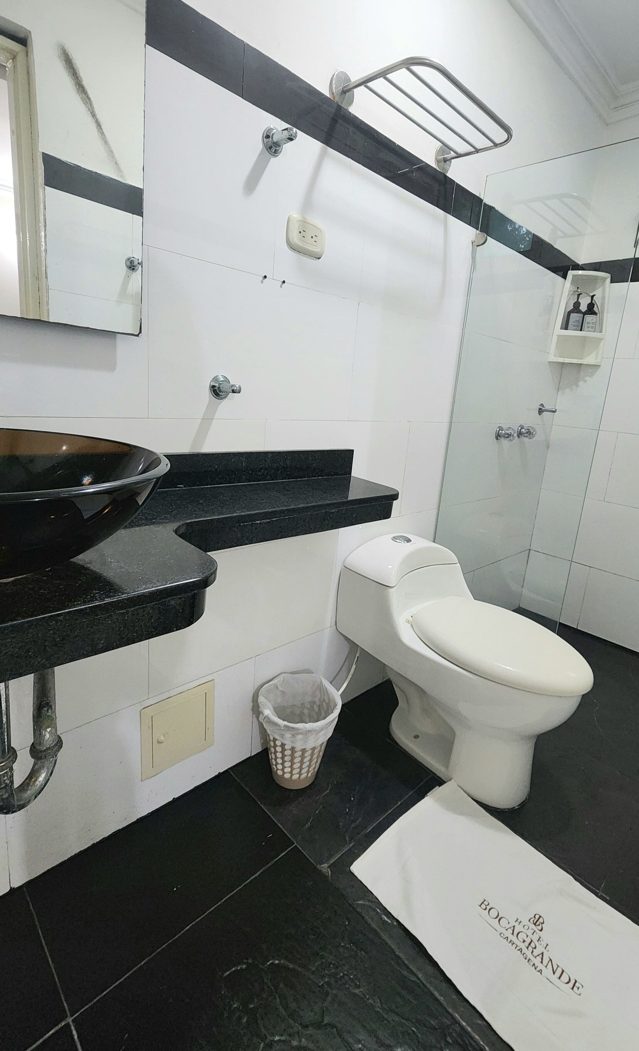 A bathroom with a black countertop sink, a white toilet, a trash bin, and a shower area.