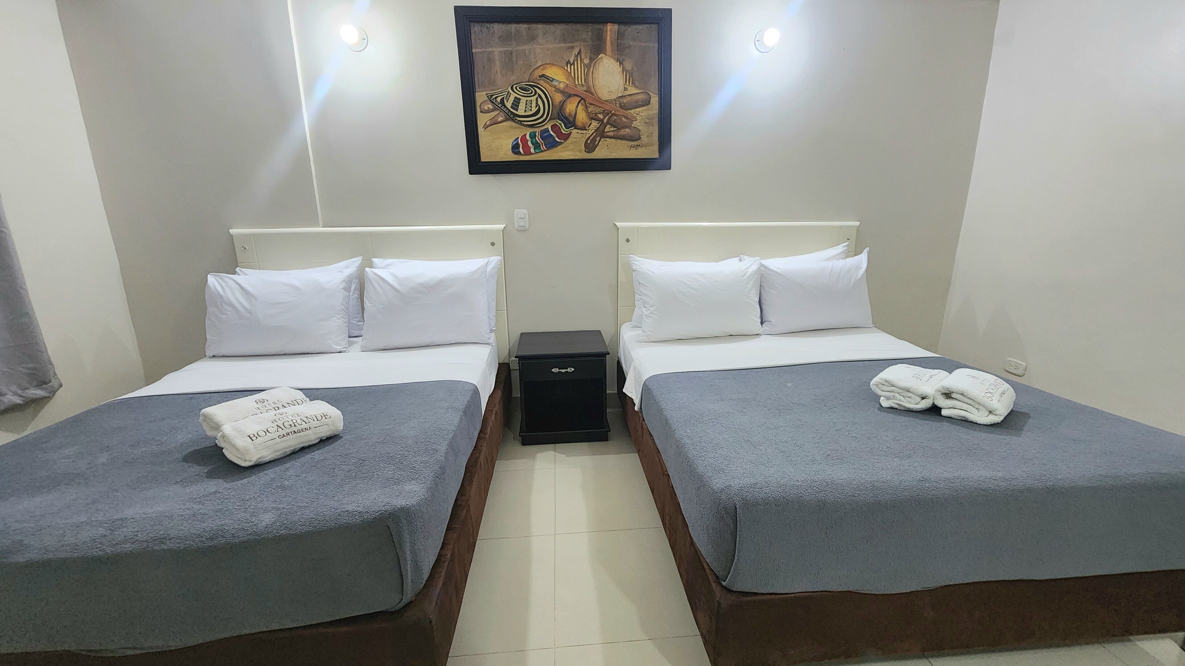 A hotel room with two beds, white bedding, a small black nightstand, and a painting on the wall.