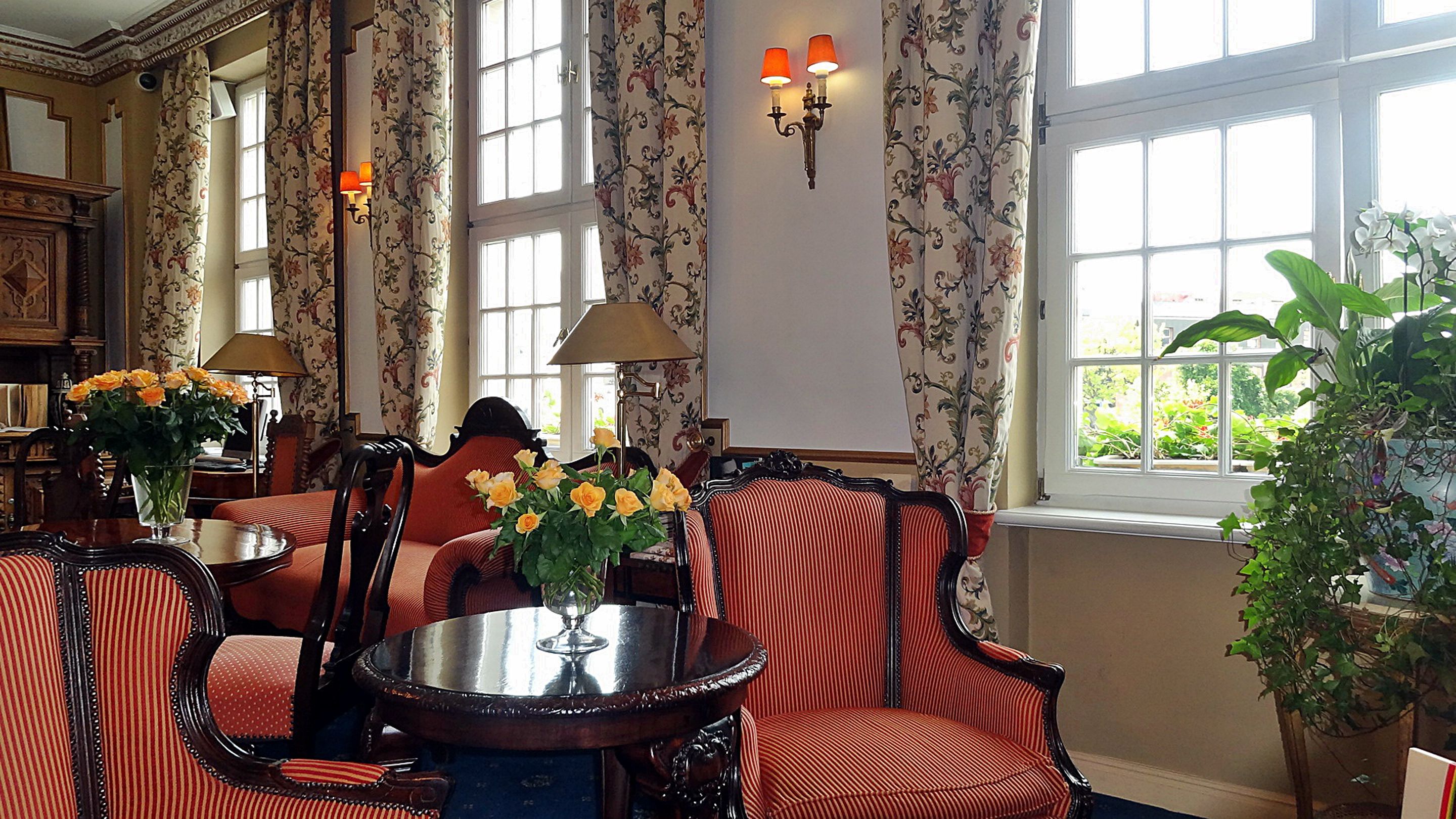 A room with a round table, striped chairs, floral curtains, and a large window with a view of greenery.