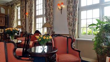 A room with a round table, striped chairs, floral curtains, and a large window with a view of greenery.