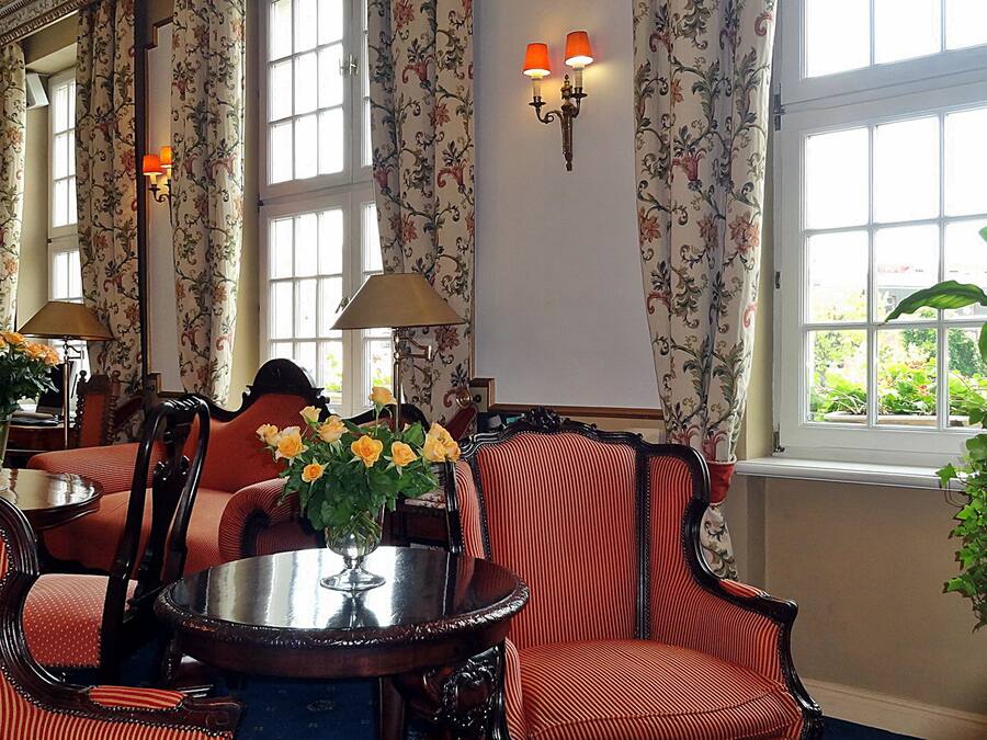 A room with a round table, striped chairs, floral curtains, and a large window with a view of greenery.