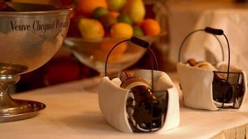 A table with a silver bowl labeled "Veuve Clicquot Ponsard," two small baskets with bottles, and a bowl of fruit in the background.