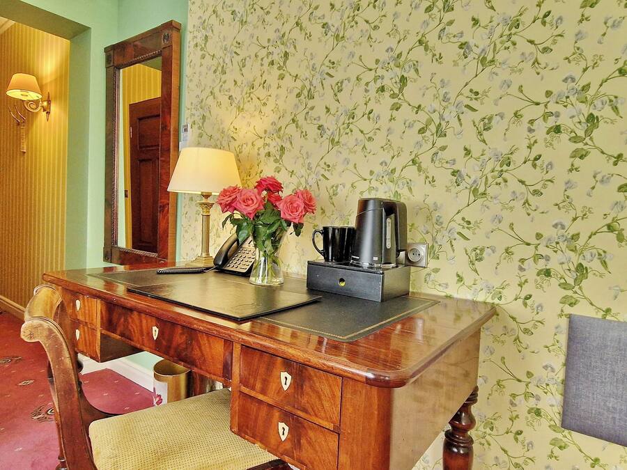 Un escritorio de madera con una lámpara, una cafetera y un florero con flores.