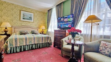 Habitación de hotel con cama, televisión, escritorio, silla, mesa y un florero con flores.