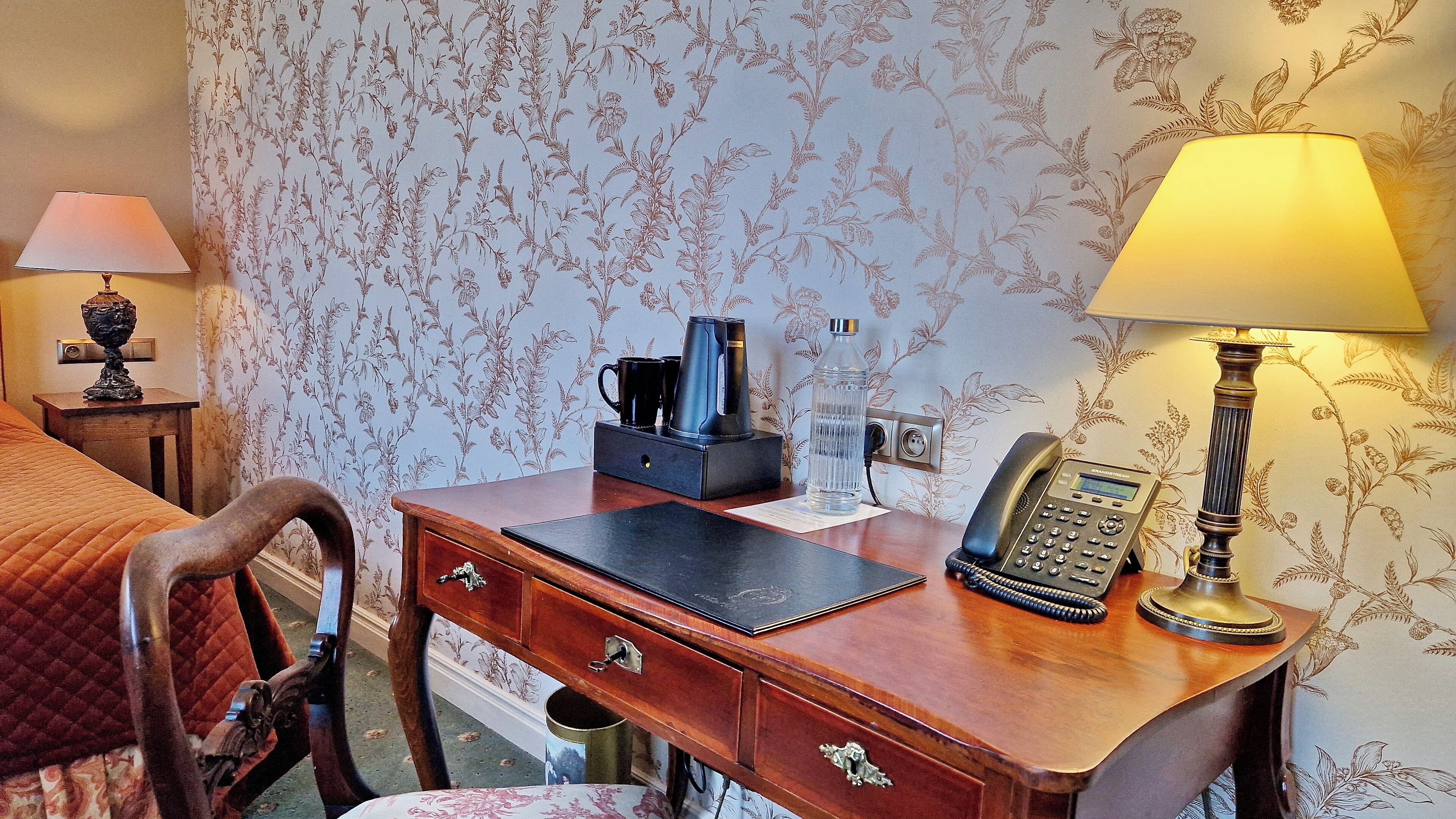Et hotelværelse med et træskrivebord, en telefon, en kaffemaskine og en lampe.