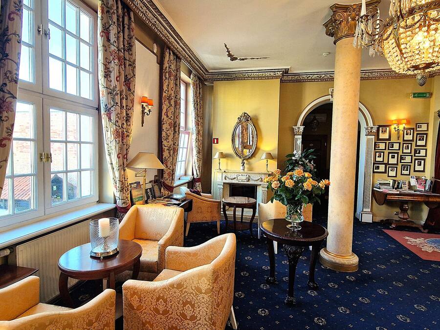 A room with a fireplace, floral curtains, a chandelier, and a carpeted floor.